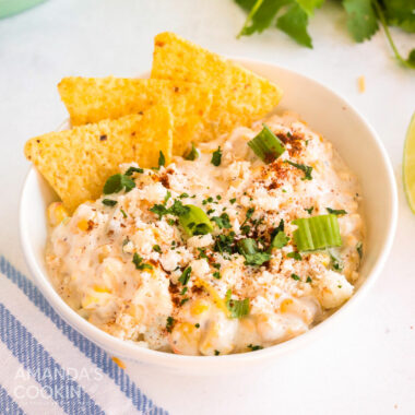 white bowl of corn dip, tortilla chips set in the dip on the side
