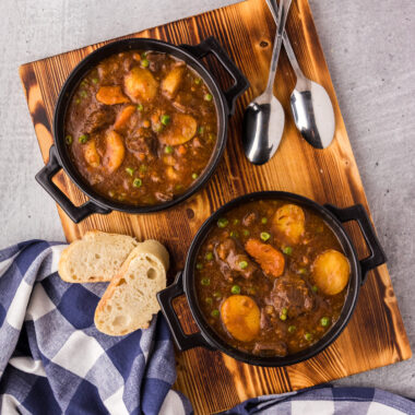 Two bowls of Instant Pot Beef Stew on a serving board with bread on the side